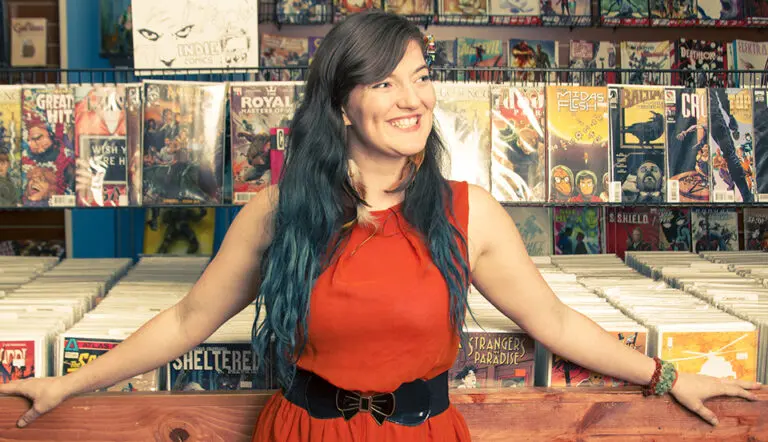 Woman in red dress leans on comic book stand while she smiles
